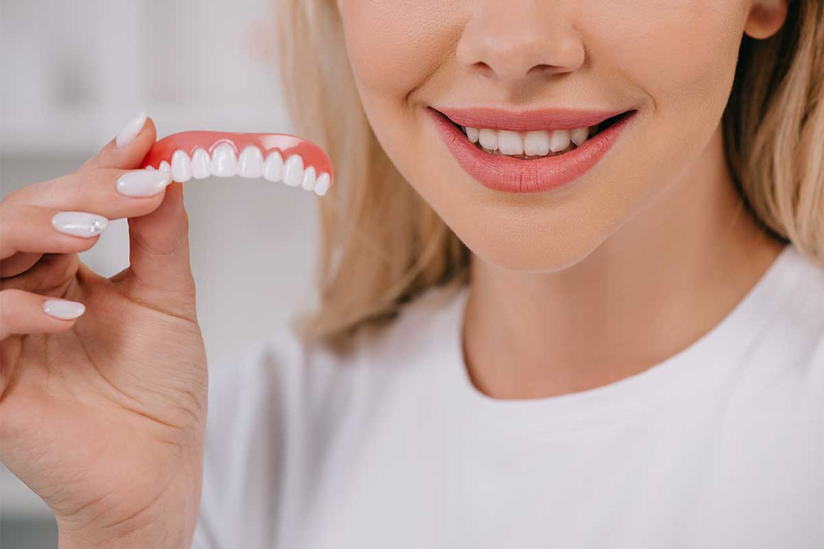 Cropped View smiling woman holding a denture