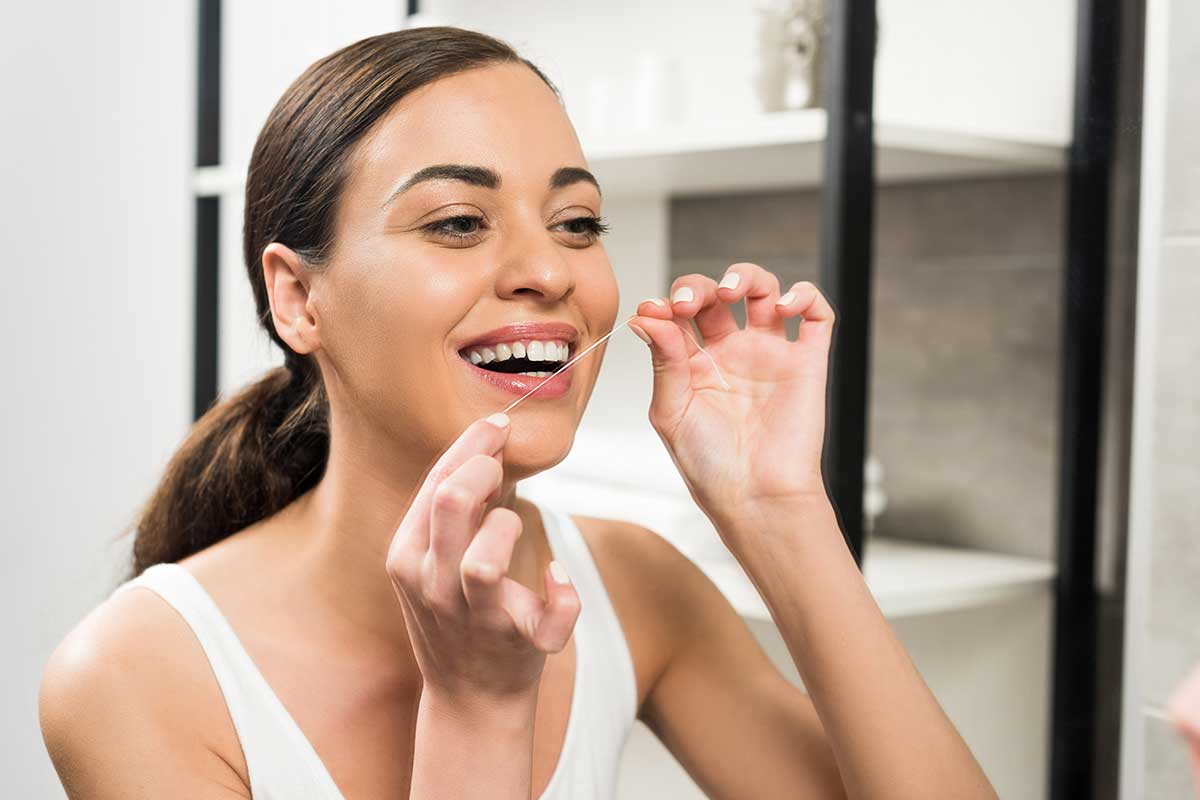 Cheerful brunette woman using dental floss in bathroom