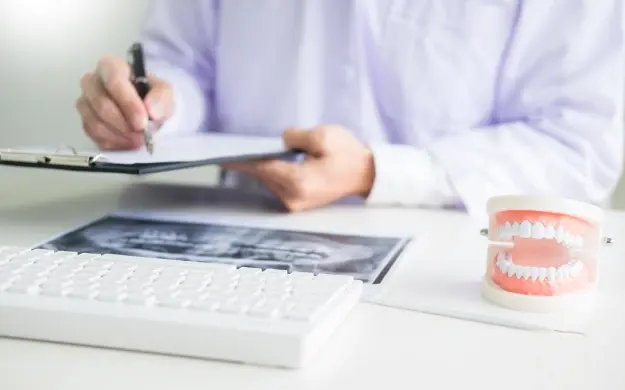 Dentist reviewing dental x-rays and insurance documentation with teeth model on desk.