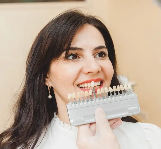 Woman smiling while holding a dental shade guide showing tooth color options for veneers.