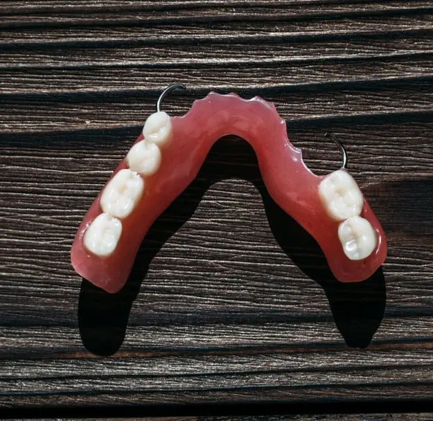 Partial denture with artificial teeth on pink acrylic base displayed on wood surface.