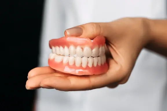 Hand holding a full denture model showing complete upper and lower teeth.