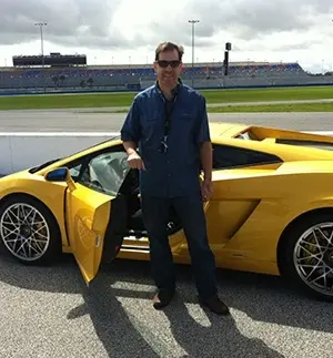 Dr. Russo stands beside a yellow sports car at a racetrack in Orlando.