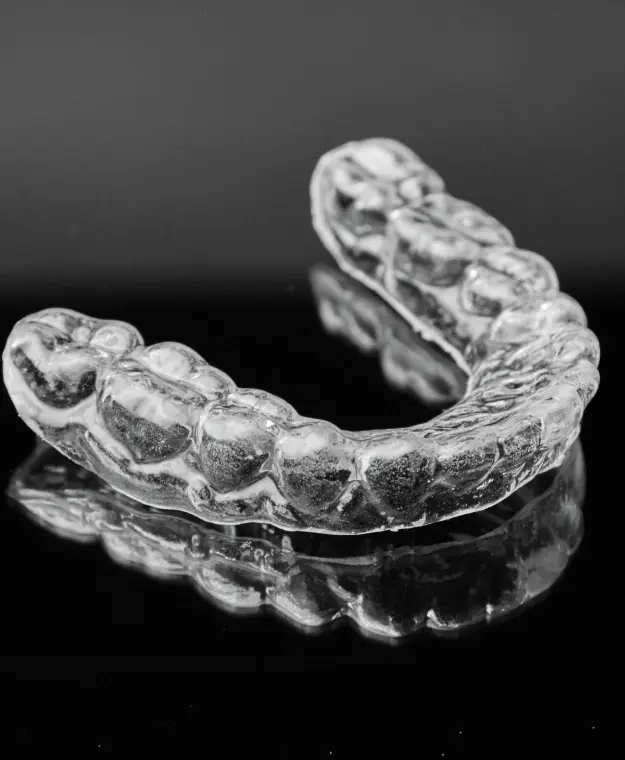 Clear dental night guard shown from two angles on reflective surface.