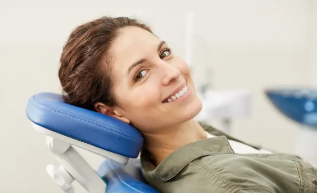 Smiling woman relaxing in dental chair with blue headrest during comfort treatment.