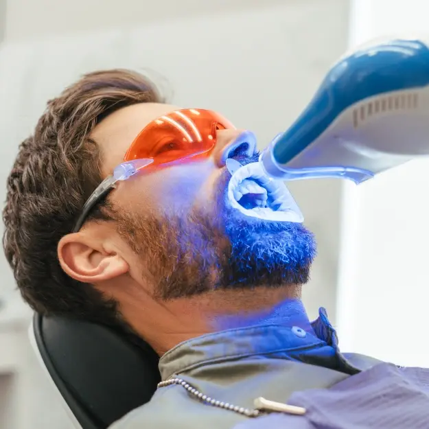 Patient receiving professional teeth whitening treatment with blue LED light technology.