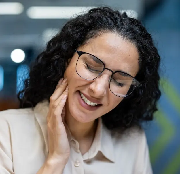 Woman wearing glasses smiling while touching her jaw during TMJ grinding therapy consultation in Orlando.