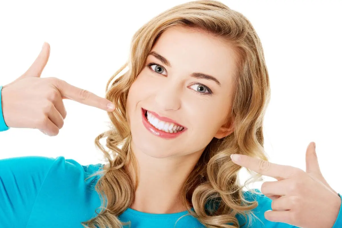 Woman with bright white smile pointing to her teeth in dental whitening promotion.