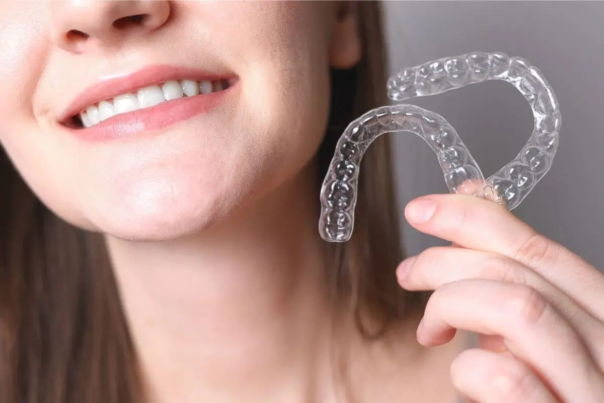 Woman smiling while holding clear Invisalign aligners near her face.