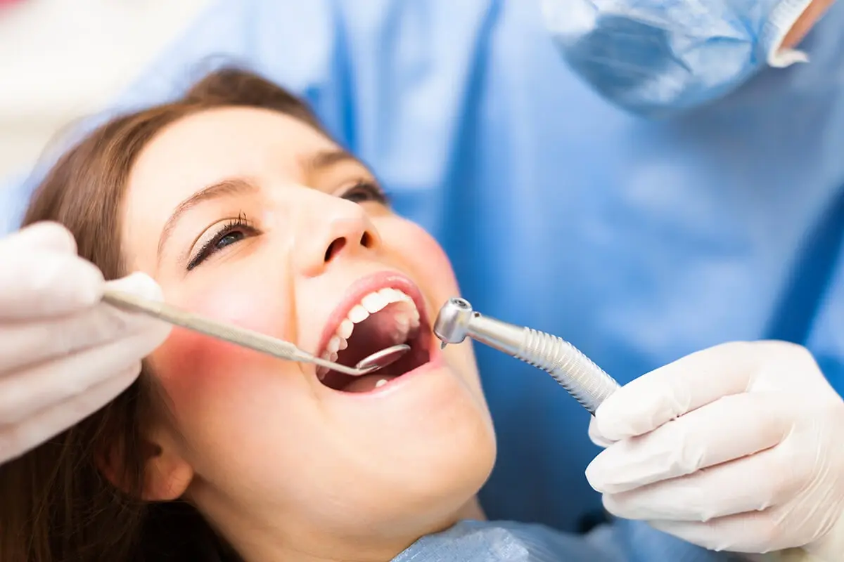 Dentist examining patient's teeth during professional dental cleaning and fluoride treatment.