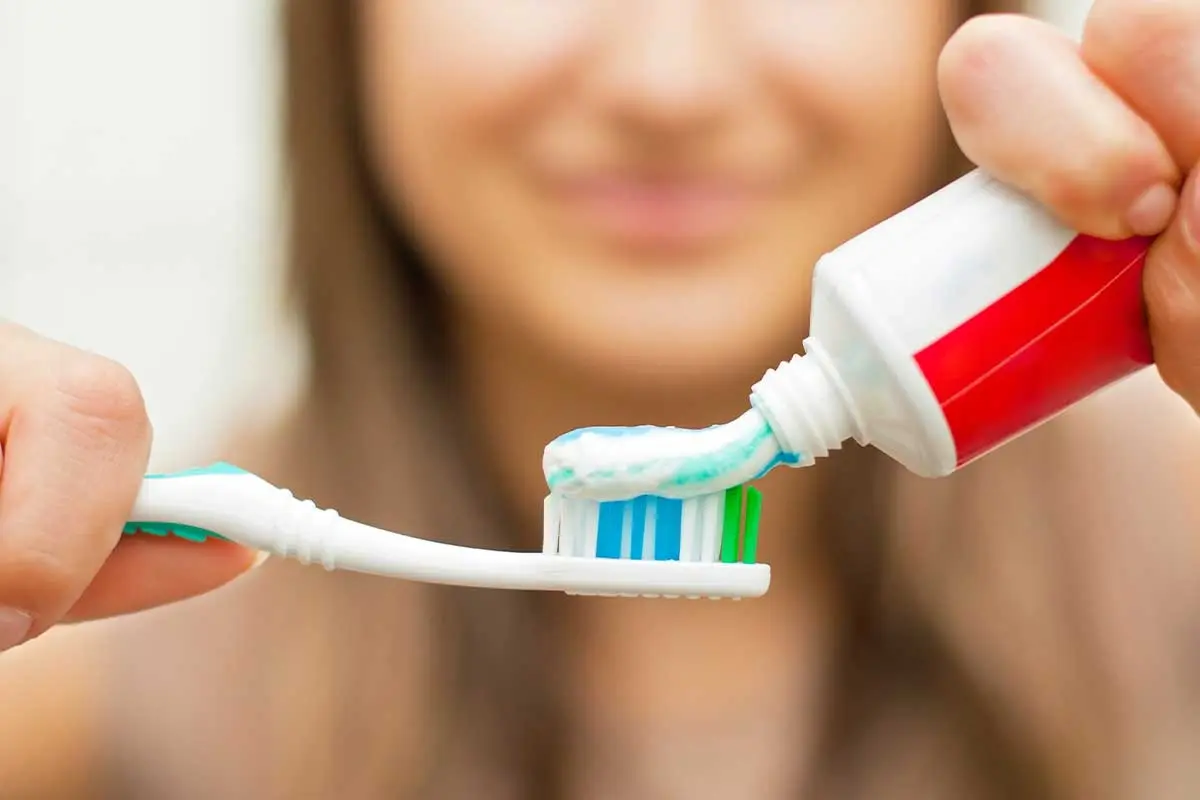 Woman squeezing toothpaste onto toothbrush for daily dental care routine.