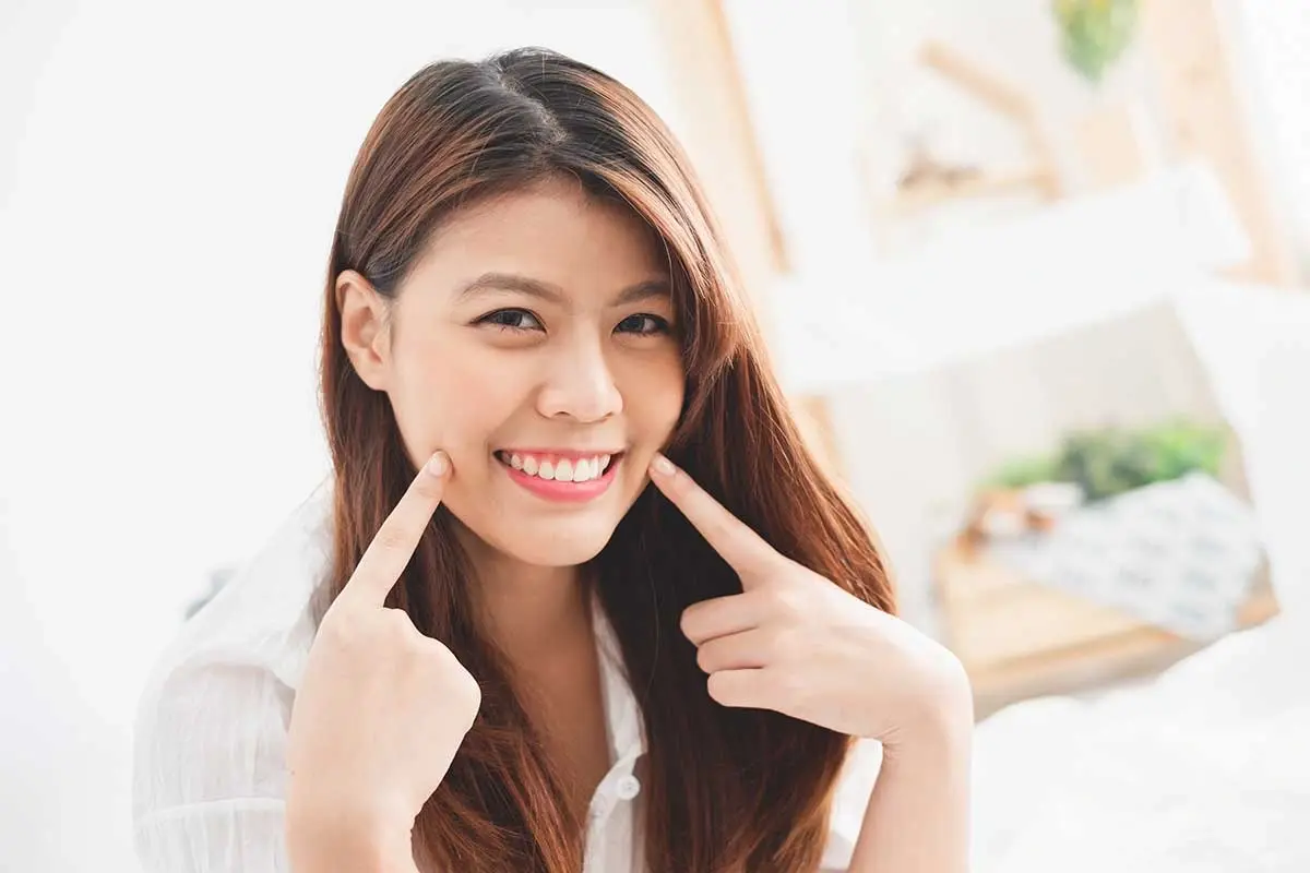 Young woman with bright smile pointing to her teeth, displaying results of dental implant treatment.