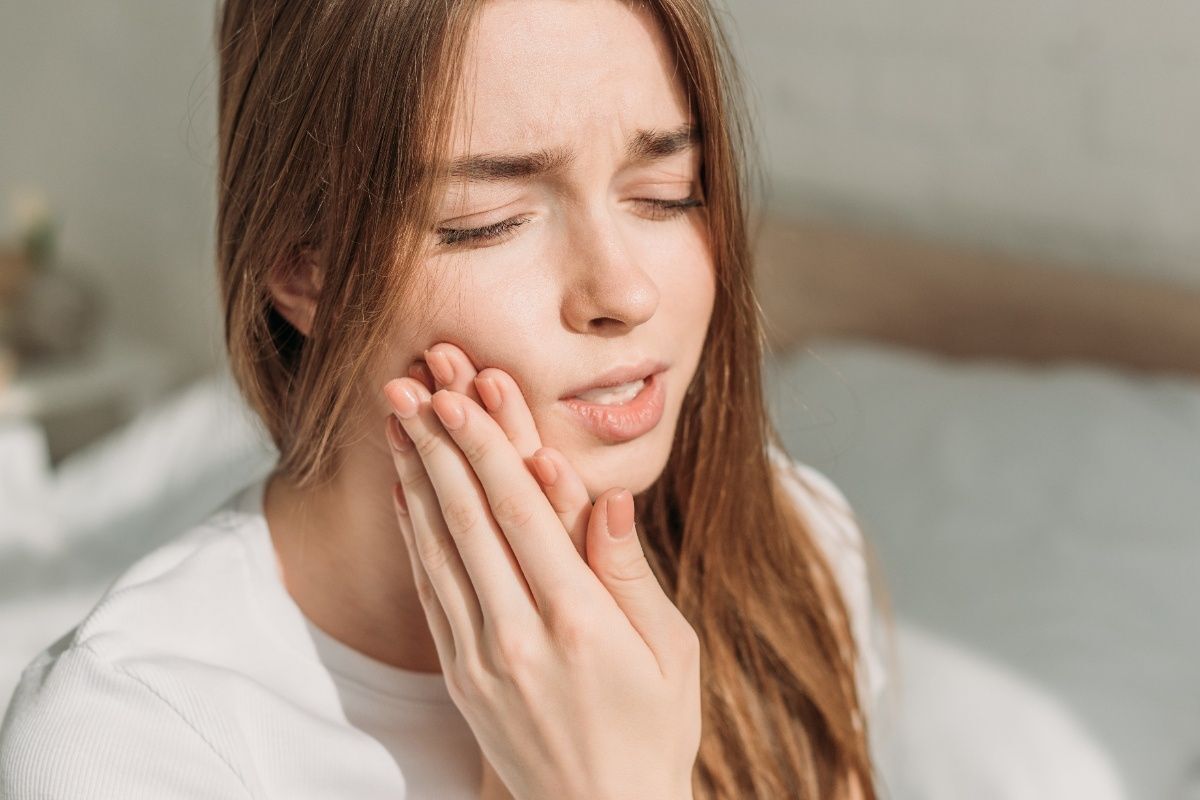 Woman with tooth pain holding her cheek, experiencing severe dental discomfort requiring emergency treatment.