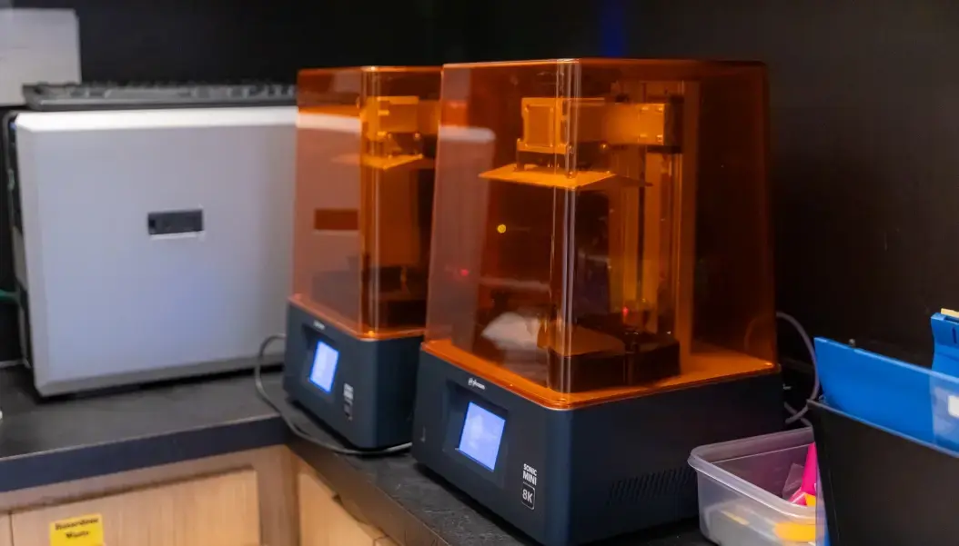Two orange 3D resin printers with digital impression technology displayed in a modern dental office.