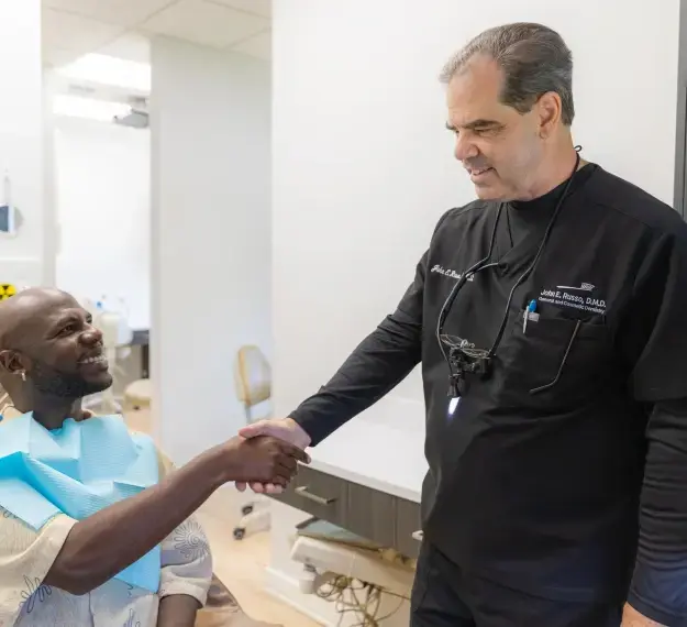 Dentist in black scrubs shaking hands with patient during oral conscious sedation consultation.