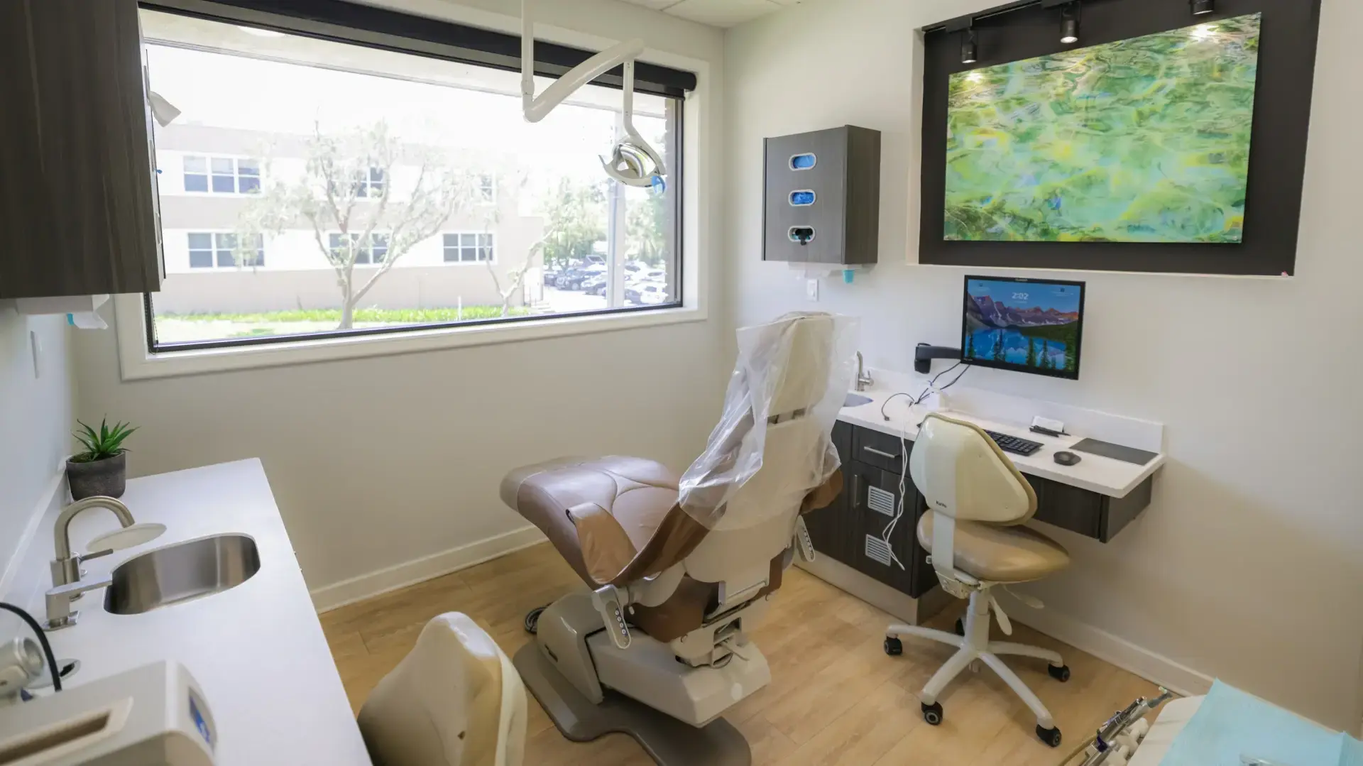 Clean and modern dental treatment room at John E. Russo DMD in Orlando FL featuring a tan dental chair overhead light computer workstation and dental instruments on a tray