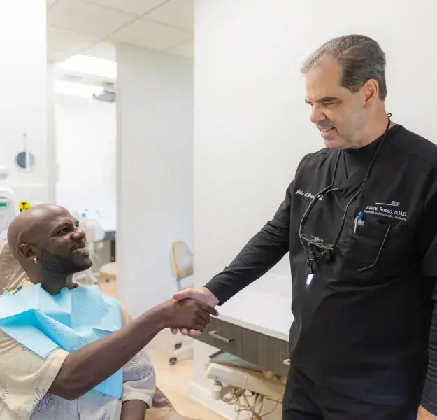 Dentist in black scrubs shaking hands with male patient during preventive dental care consultation in Orlando office.
